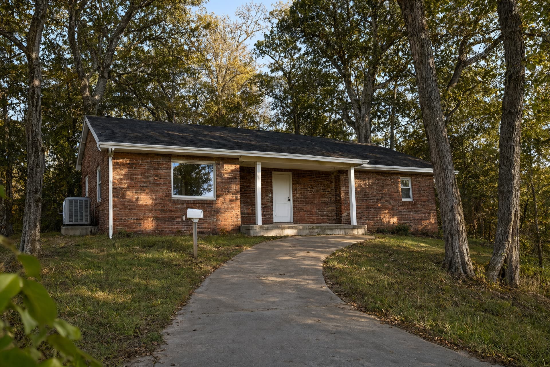 Brick ranch house on a wooded hillside with tall oaks and hickories, like the ridge lots around Harrisburg, AR