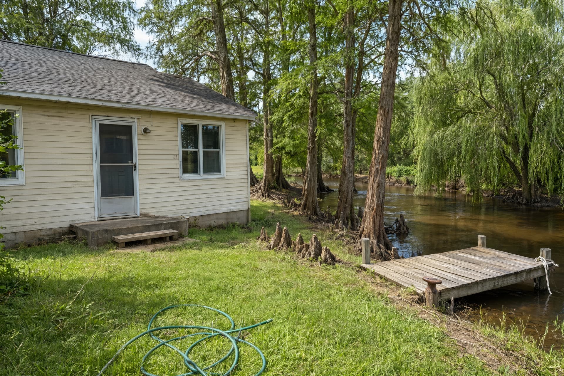 Modest home near a slow river lined with cypress and willow trees, like the river country around Lake City, AR